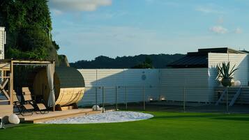 A well-maintained lawn with a wooden deck and lounge chairs, a large white building with a flat roof, and a fenced area with a circular white space.