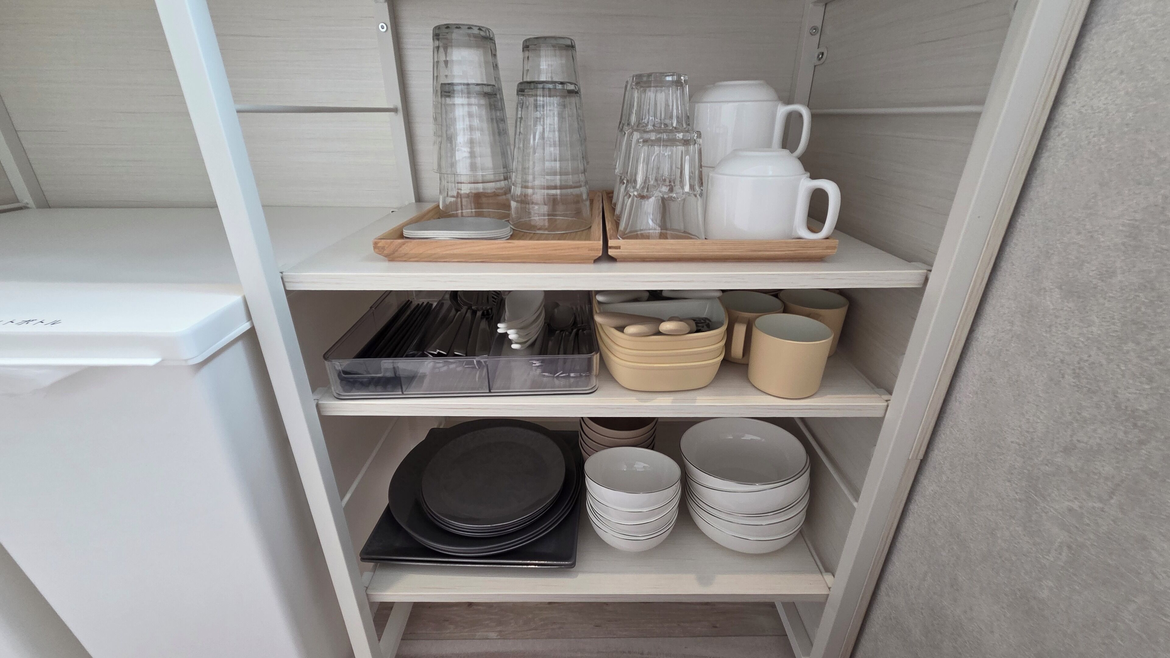A kitchen shelf with glassware, mugs, and stacked plates.