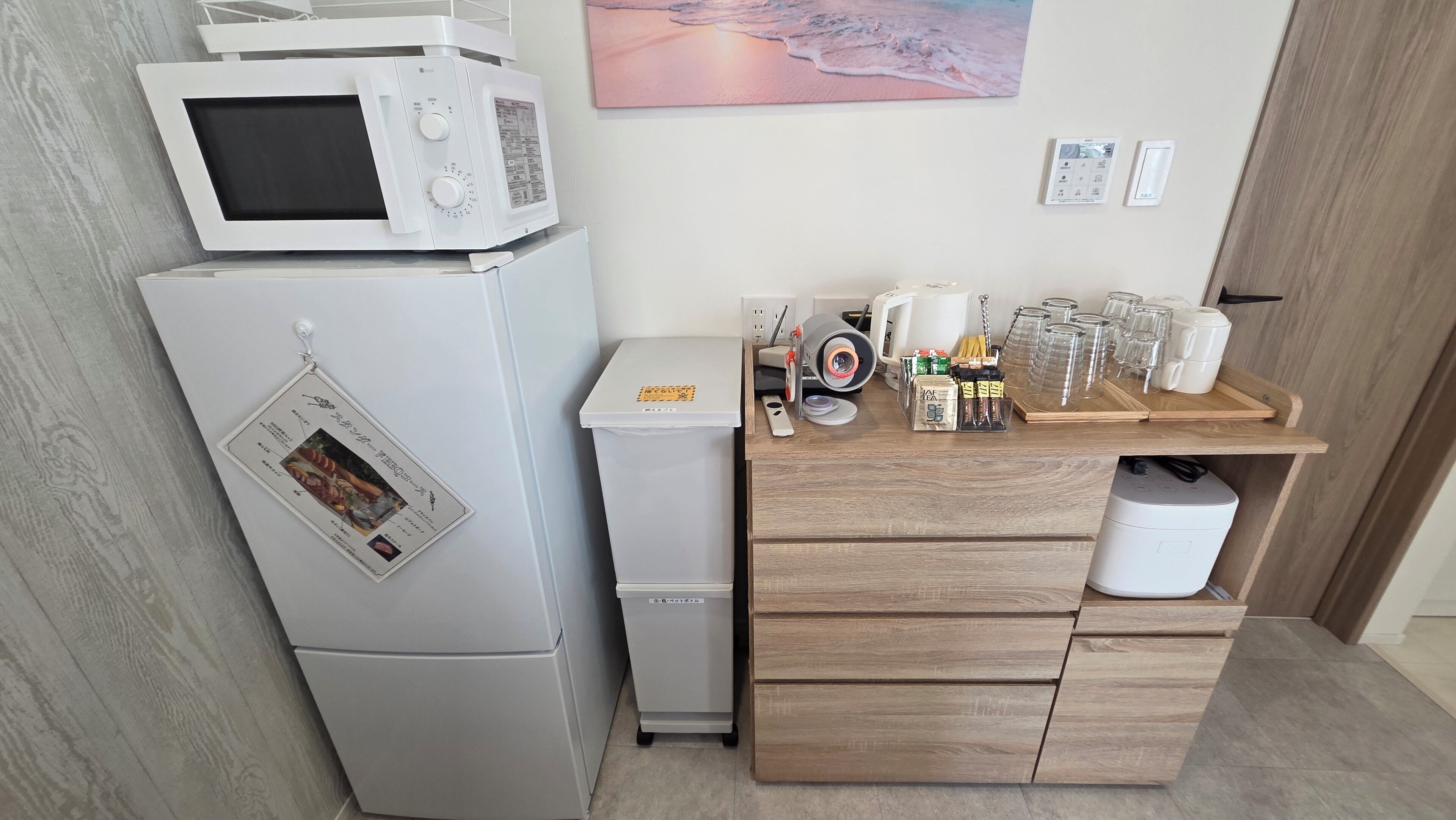 Una kitchenette compacta con microondas, refrigerador y una pequeña cafetera sobre una encimera de madera.