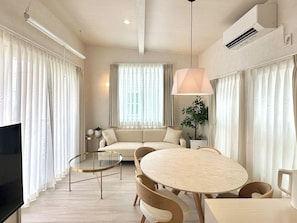 Una sala moderna con un sofá, una mesa redonda de comedor, sillas, un televisor y una planta en maceta.