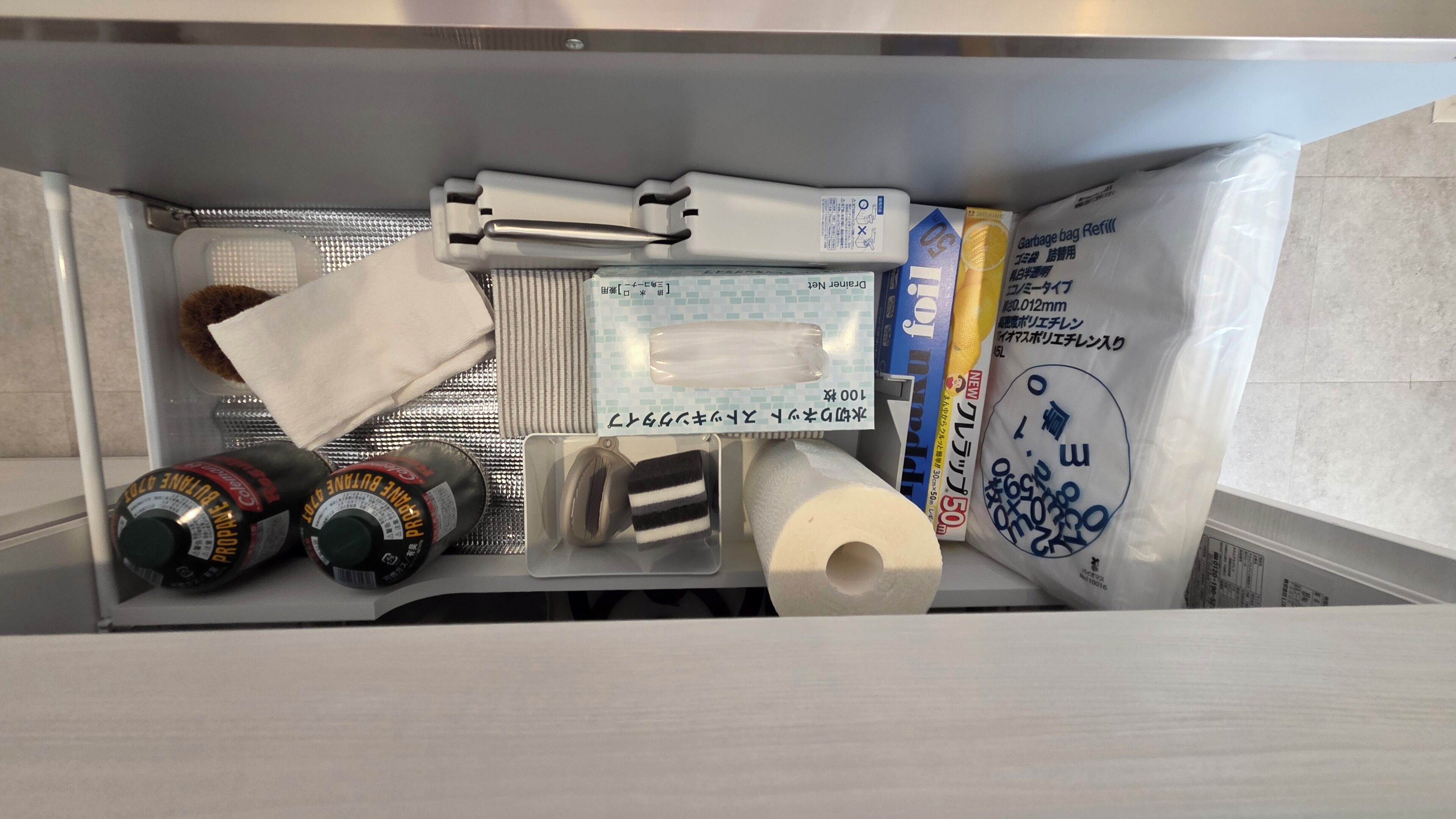 Un área de almacenamiento con diversos objetos, incluyendo una botella, un rollo de toallas de papel, una bolsa de plástico y una caja.
