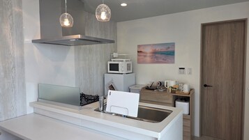 Una cocina moderna con estufa a gas, microondas y pileta. Hay luces colgantes, un cuadro en la pared y una puerta de madera.