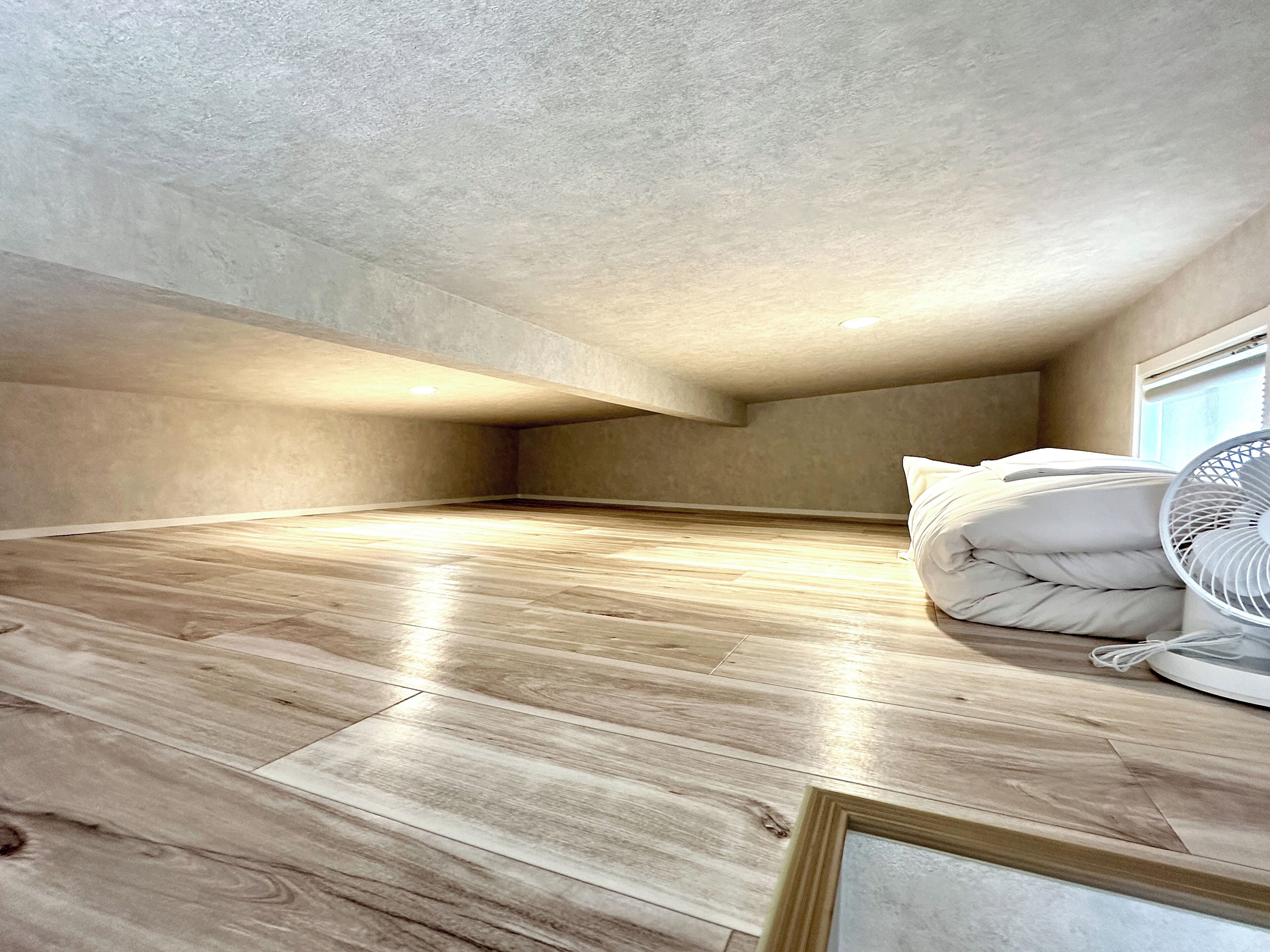 A room with a sloped ceiling, wooden flooring, and a white fan.