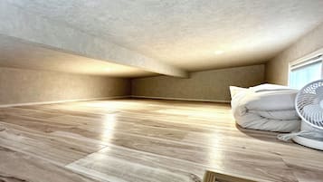 A room with a sloped ceiling, wooden flooring, and a white fan.