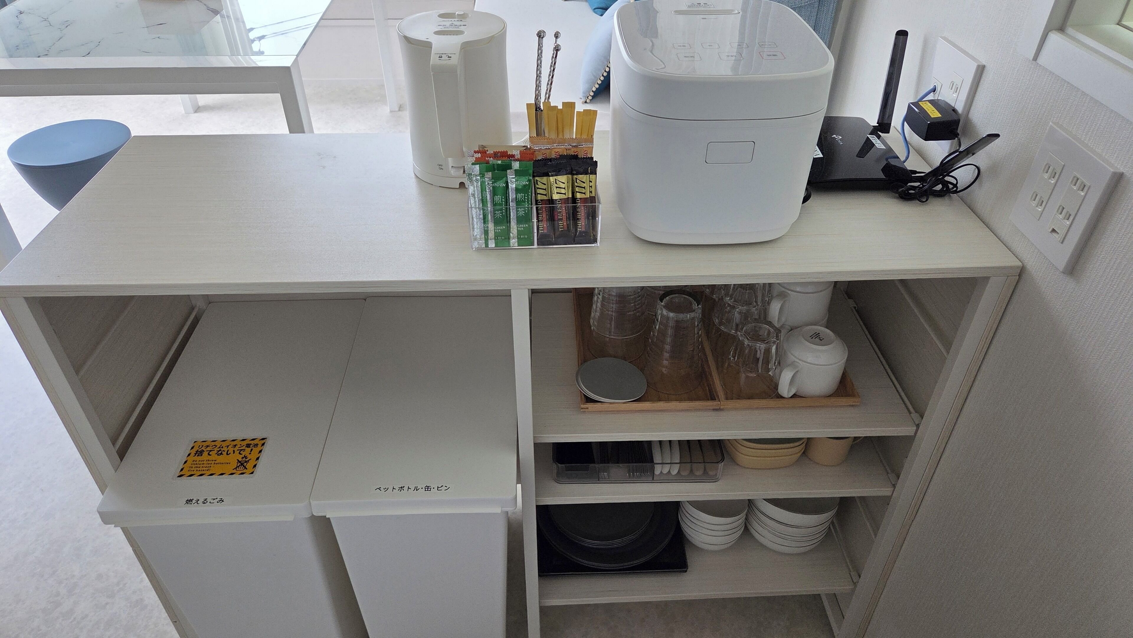 A kitchen area with a white countertop, a coffee maker, a set of chopsticks, and a tray with cups and plates.