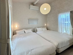 Habitación de hotel con dos camas, ventilador de techo, unidad de aire acondicionado y ventana con cortinas.