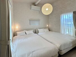 Habitación de hotel con dos camas, ventilador de techo, unidad de aire acondicionado y ventana con cortinas.