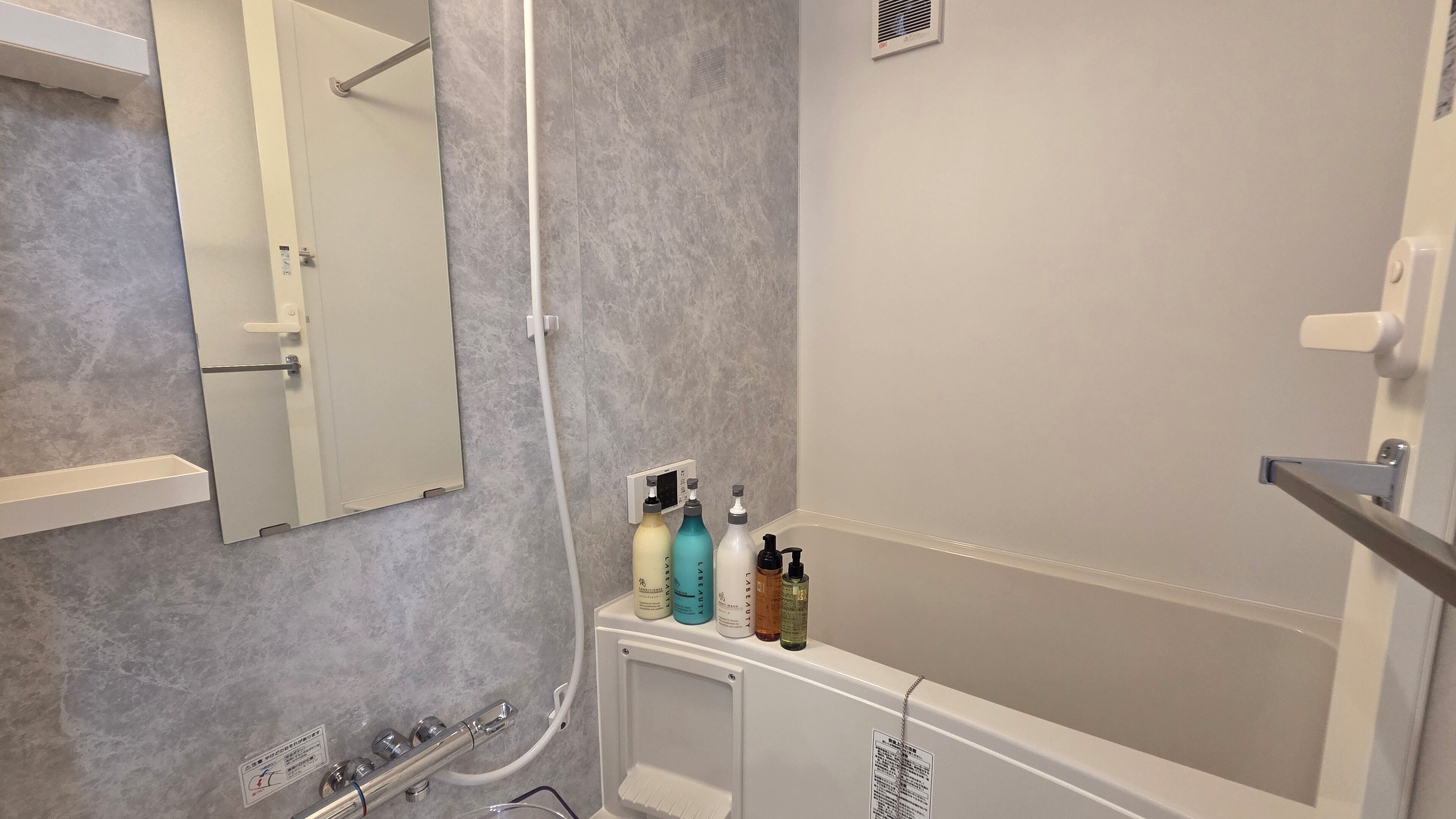 A bathroom with a bathtub, a shower, a mirror, and a shelf with toiletries.