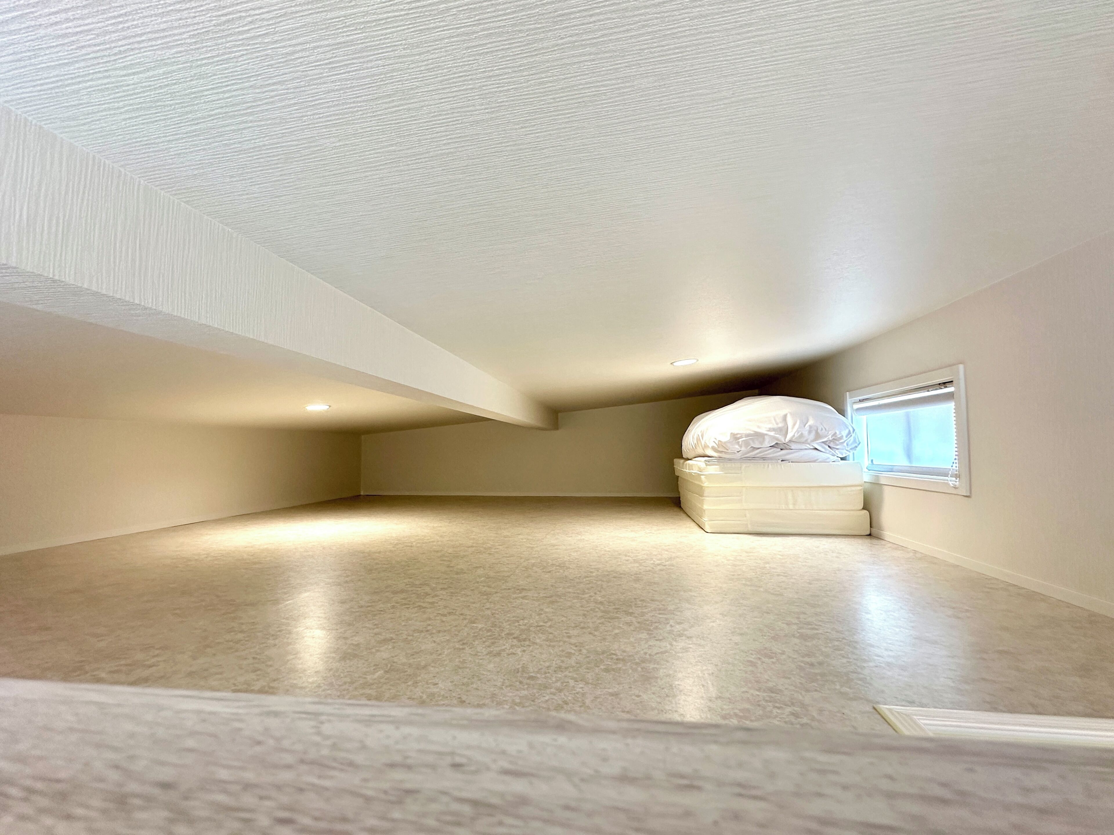 A spacious attic bedroom with a single bed, a window with blinds, and a sloped ceiling.