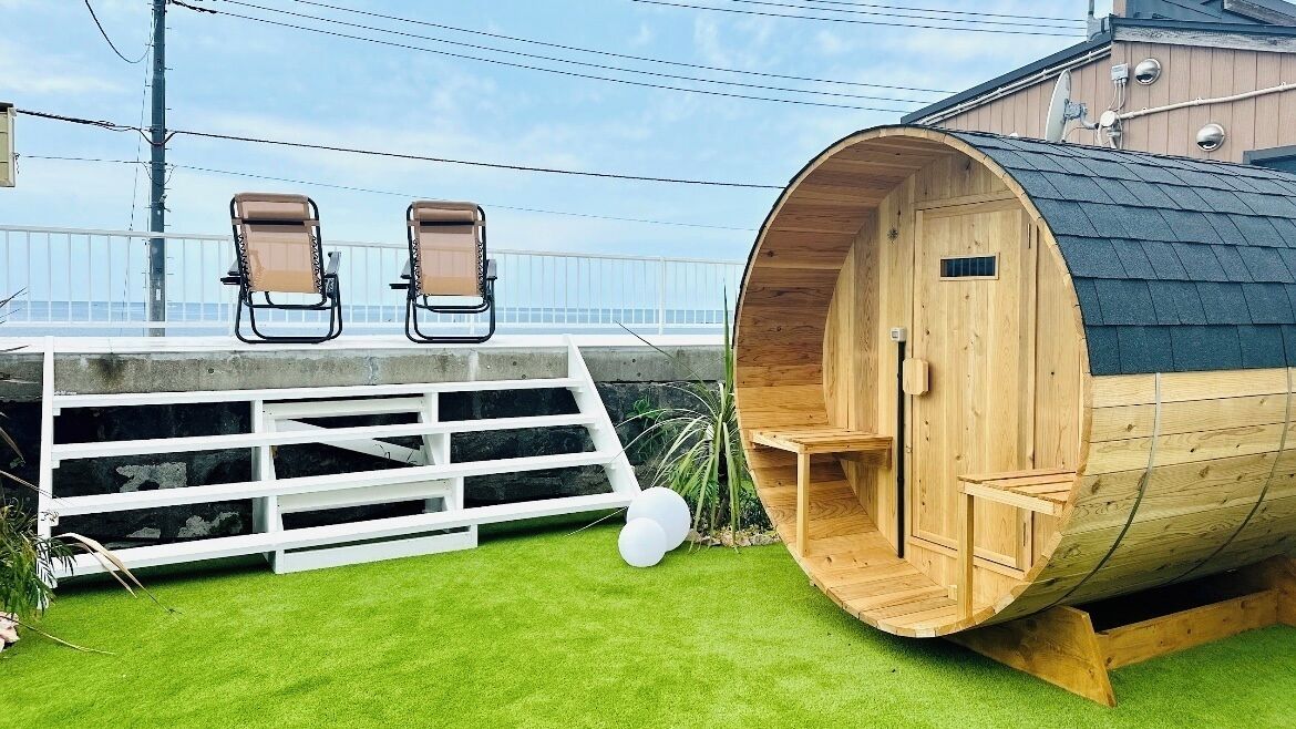 A sauna with a wooden exterior and a white deck with two chairs.