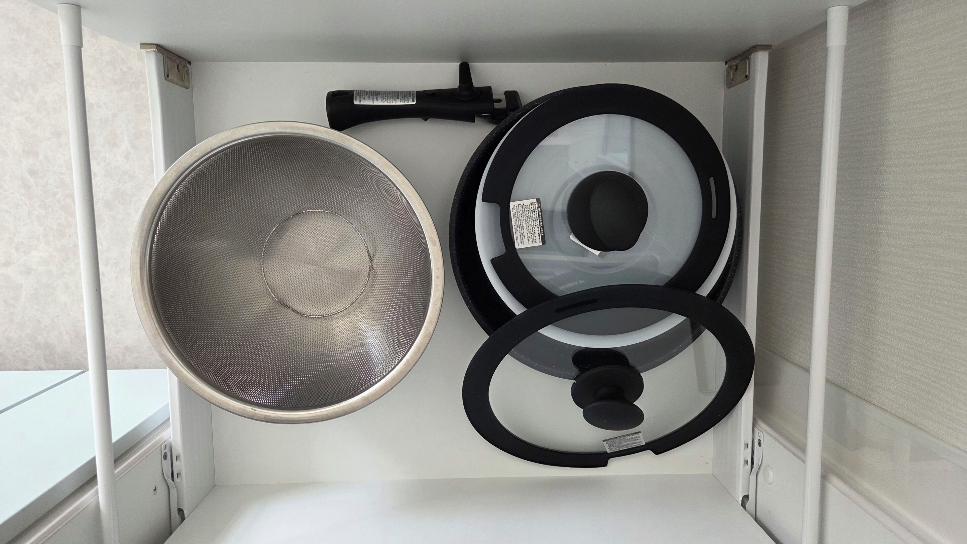 A white cabinet with a metal mesh basket and two black circular objects, possibly kitchen appliances.