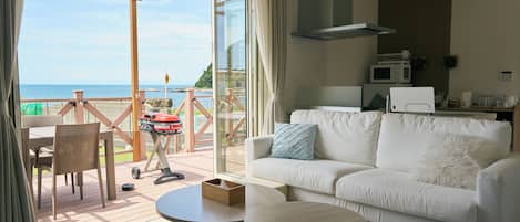 A modern living room with a white sofa, a round coffee table, and a view of the sea through large glass doors.