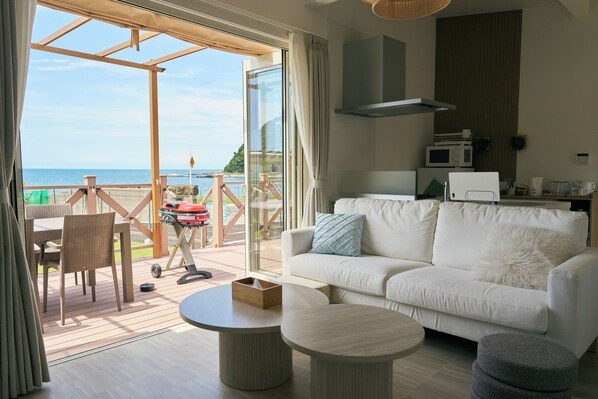 Un salon moderne avec un canapé blanc, une table basse ronde et une vue sur la mer grâce à de grandes portes vitrées.