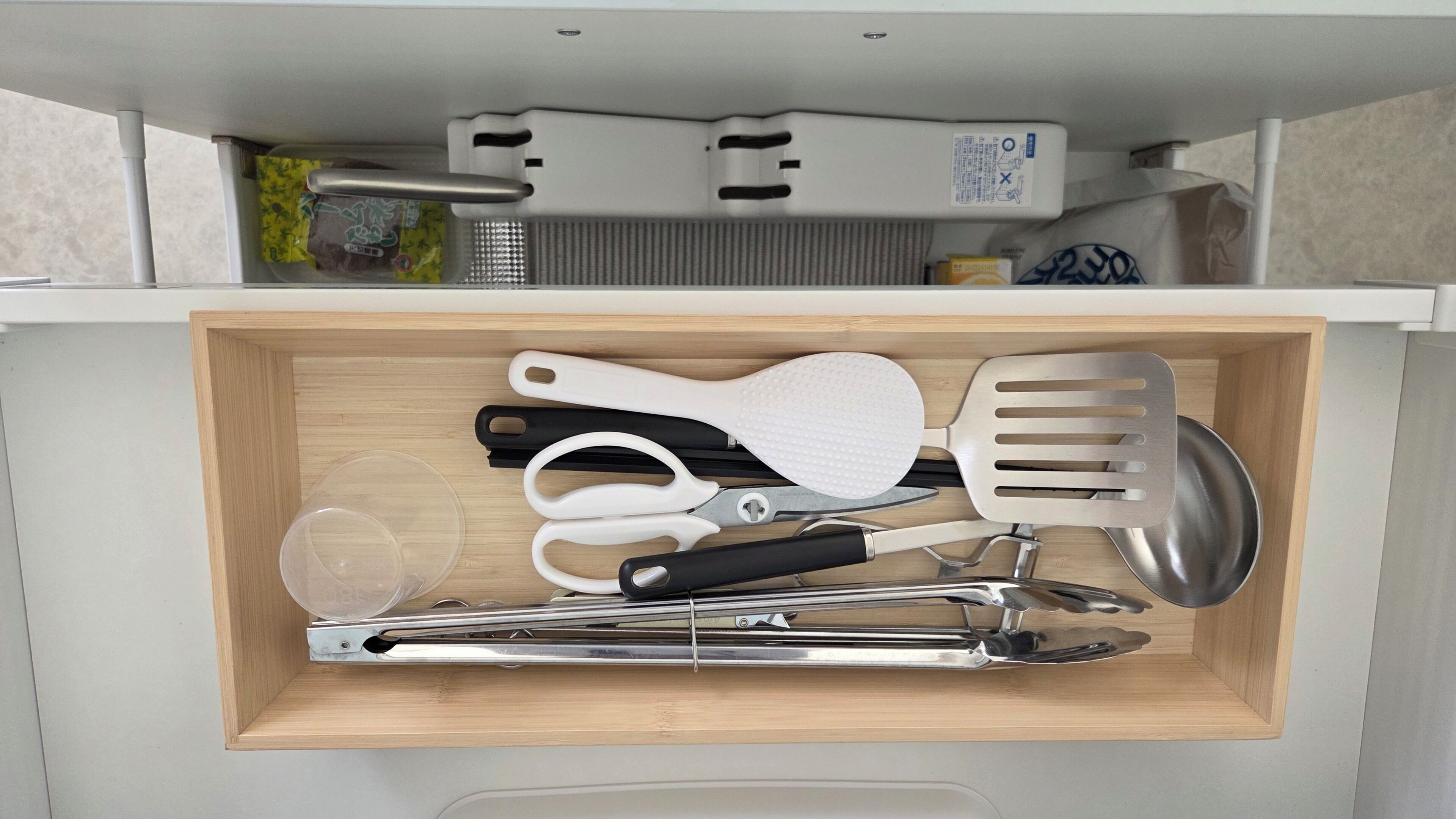 A drawer containing kitchen utensils including a spatula, tongs, and a pair of scissors.