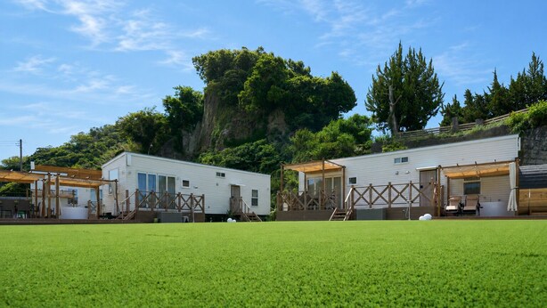 Un camping con casas móviles, un campo cubierto de césped y una colina boscosa al fondo.