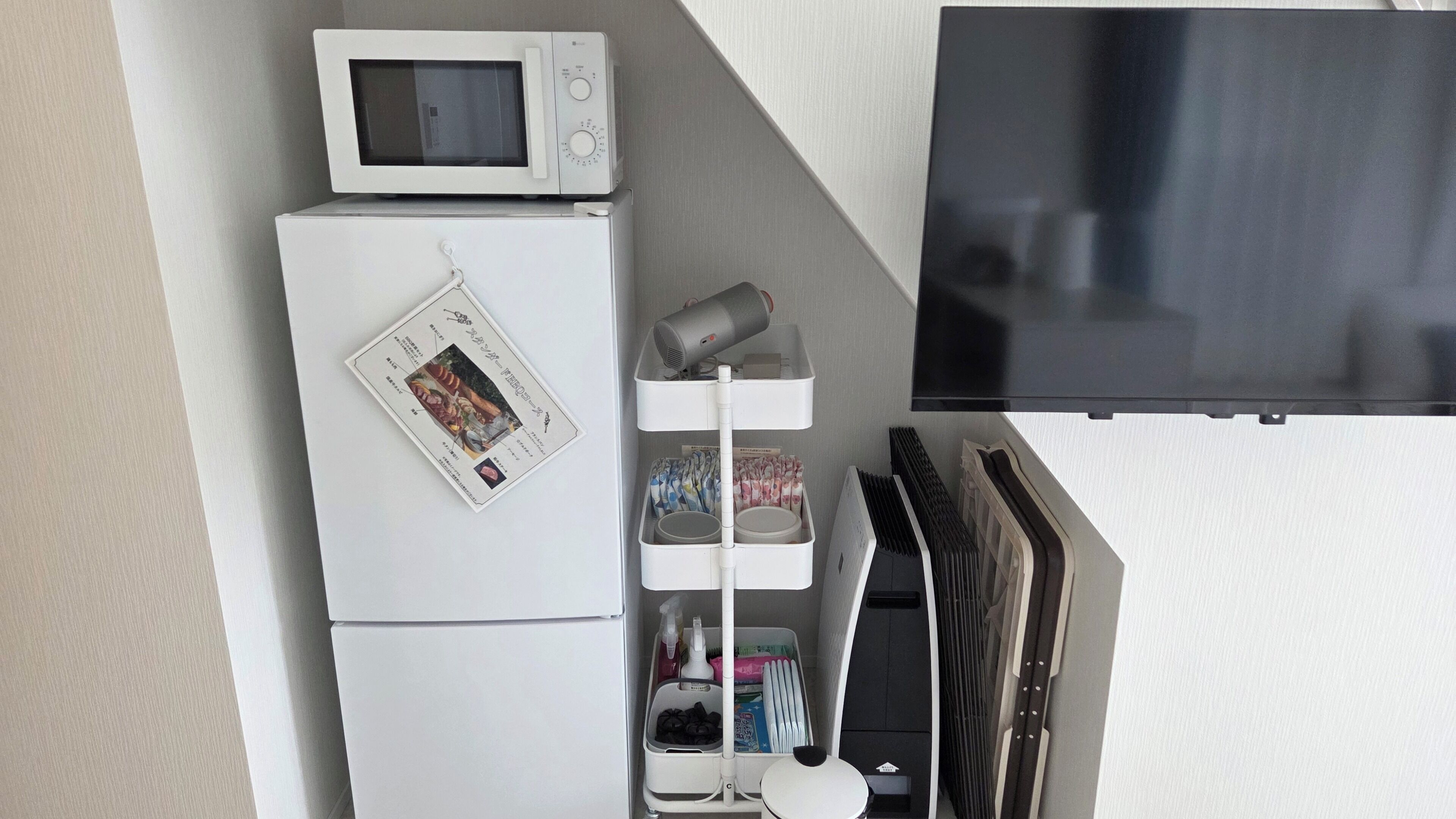 Una kitchenette compacta con microondas, refrigerador y un pequeño estante con utensilios de cocina.