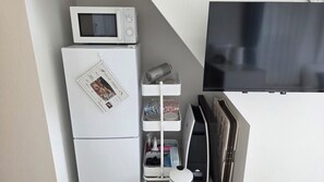 Una kitchenette compacta con microondas, refrigerador y un pequeño estante con utensilios de cocina.