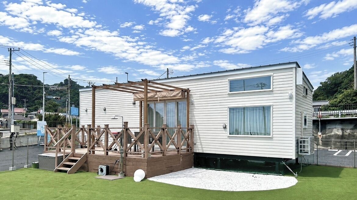 Una casa móvil con terraza de madera, un porche pequeño y un patio cercado.