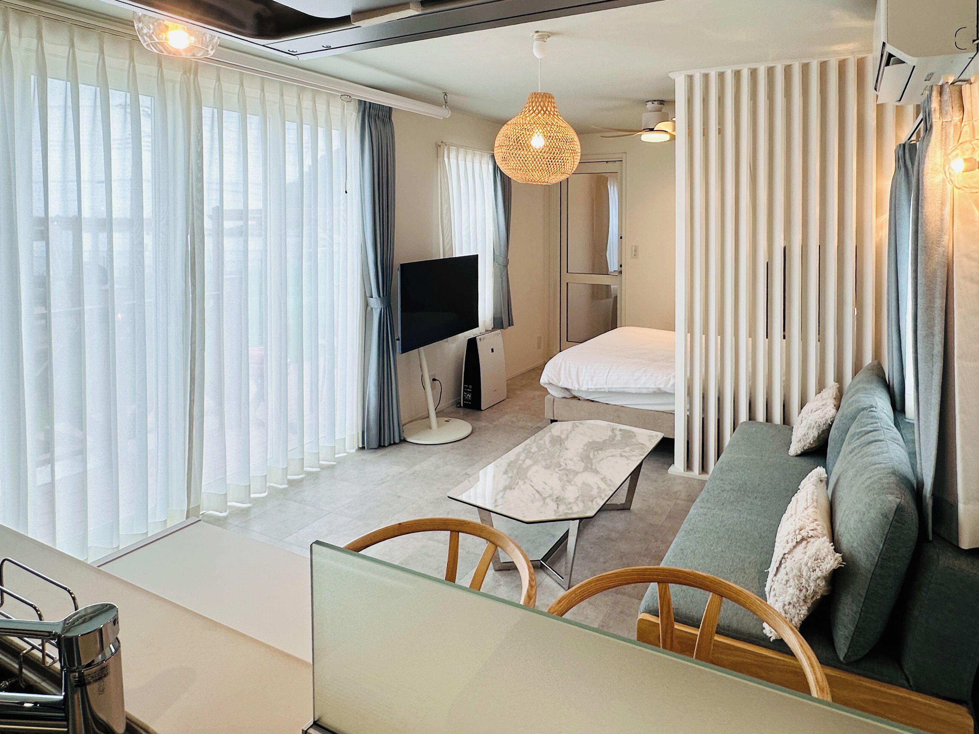 A modern living room with a sofa, a glass coffee table, a flat-screen TV, and a decorative woven light fixture.