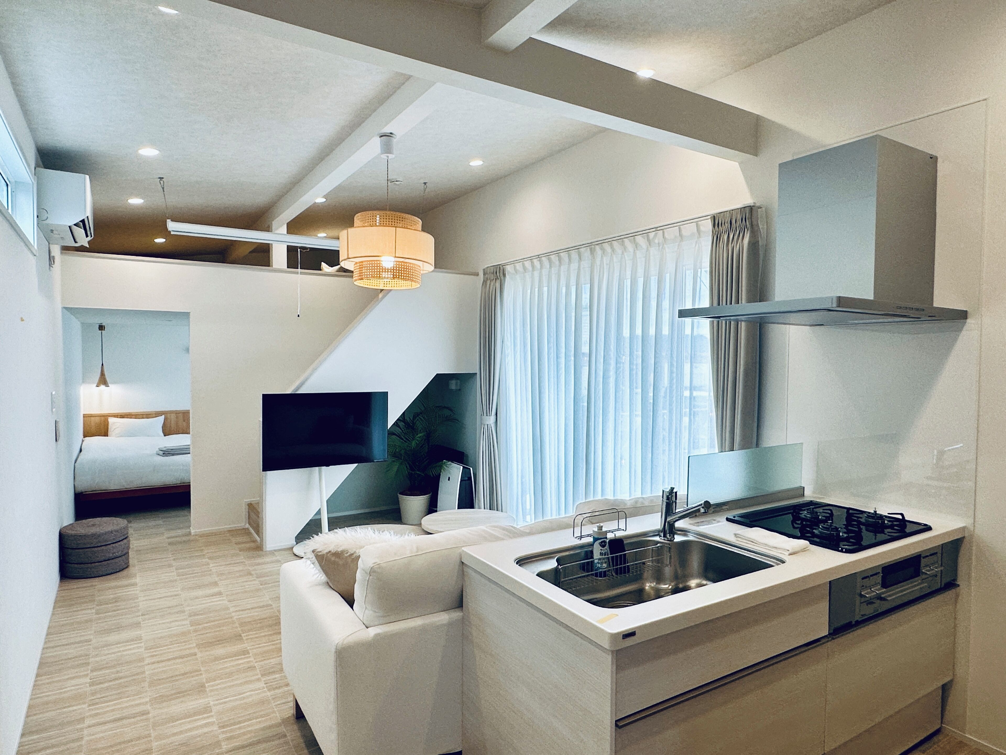 A modern kitchen with a built-in stove, a sink, and a dining area with a sofa and a television.