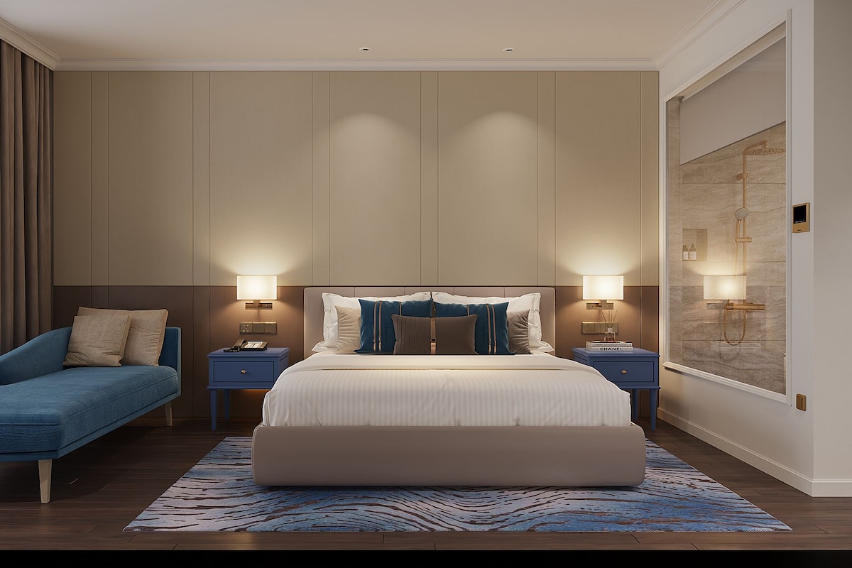 A modern hotel room with a large bed, two bedside tables, a sofa, and a large window.