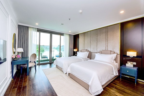 A hotel room with two beds, a desk with a chair, a TV, and a large window with a view.