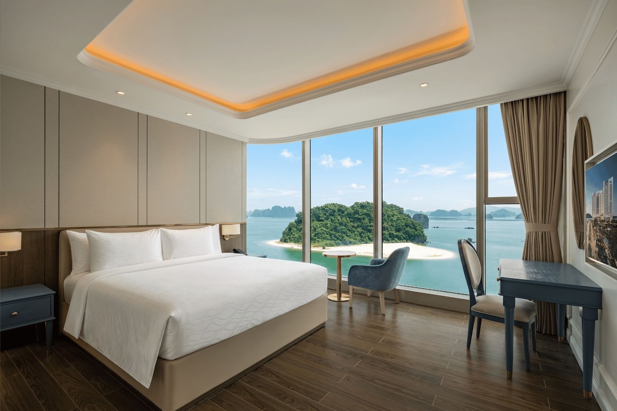 A modern hotel room with a large bed, a desk, and a view of a tropical island.
