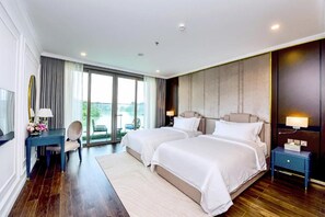 Habitación de hotel con dos camas, un escritorio, una silla, una mesita de noche y un ventanal grande.