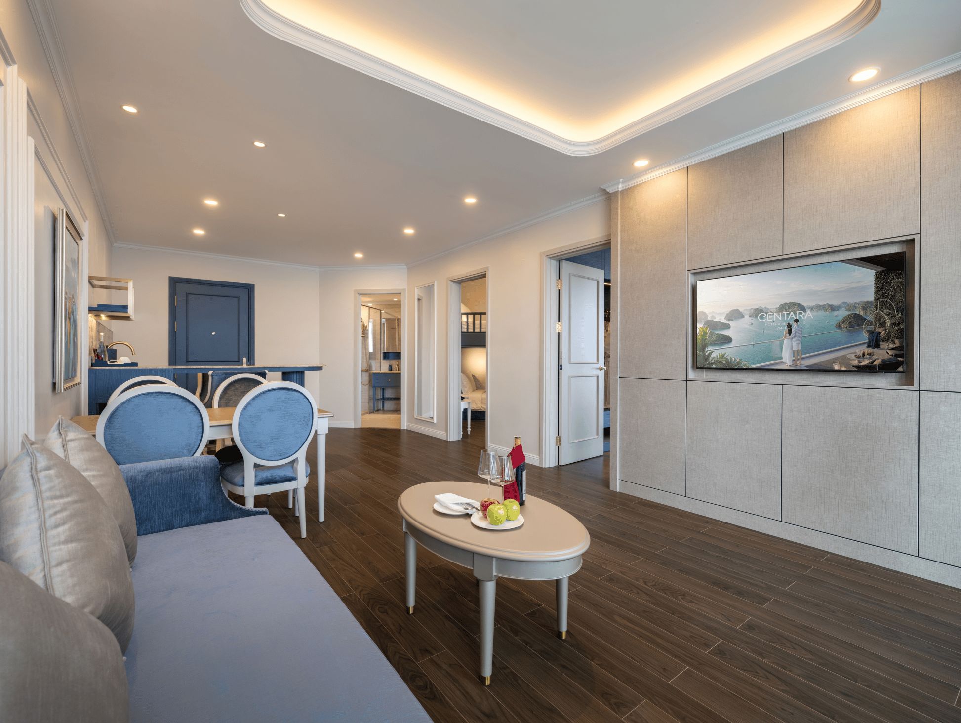 A modern living room with a sofa, chairs, a dining table, and a TV mounted on the wall.