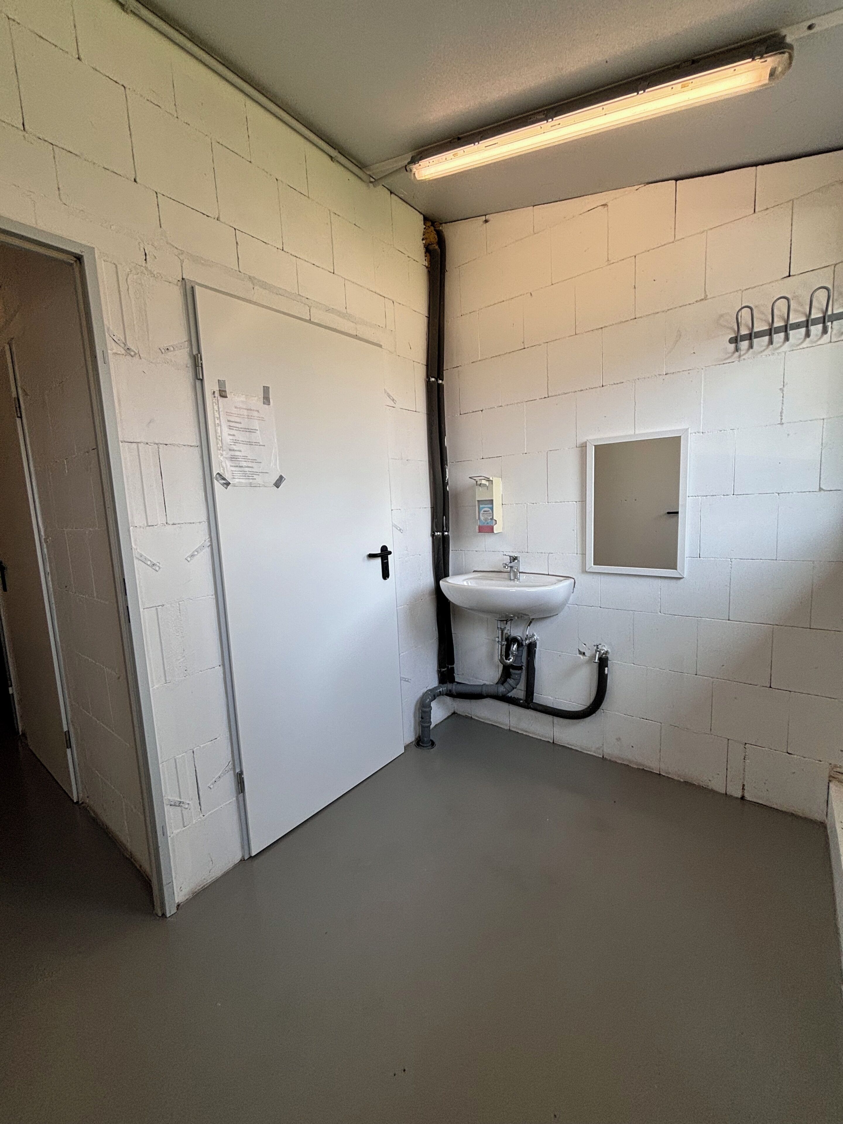 A restroom with white brick walls, a white sink, and a door with a notice taped to it.
