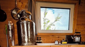 A compact kitchen with a built-in refrigerator, a window with a view of greenery, and a stove. - Tinyhouse idyll: nature & chickens (Aurich)
