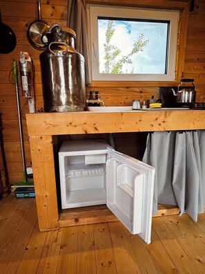 A compact kitchen with a built-in refrigerator, a window with a view of greenery, and a stove. - Tinyhouse idyll: nature & chickens (Aurich)