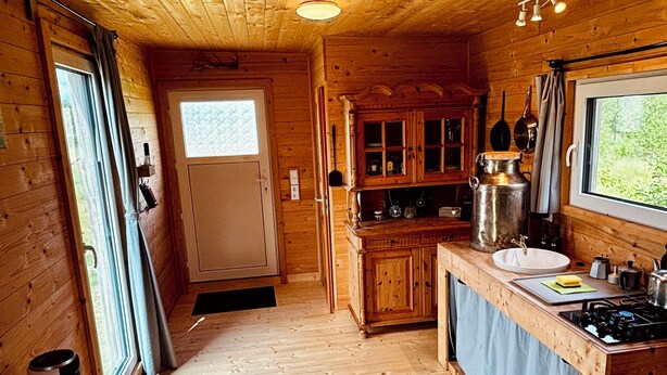 A wooden cabin interior with a kitchen area, a dining table, and a window. - Tinyhouse idyll: nature & chickens (Aurich)