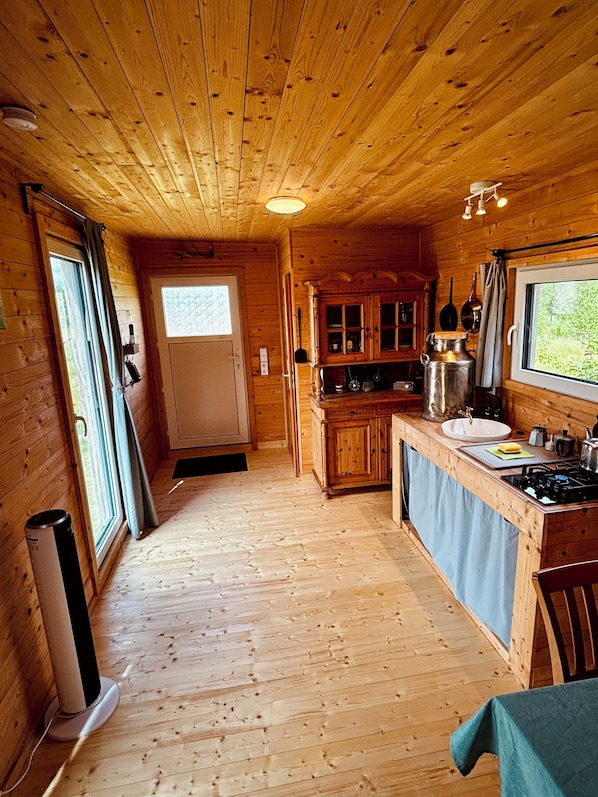 A wooden cabin interior with a kitchen area, a dining table, and a window. - Tinyhouse idyll: nature & chickens (Aurich)
