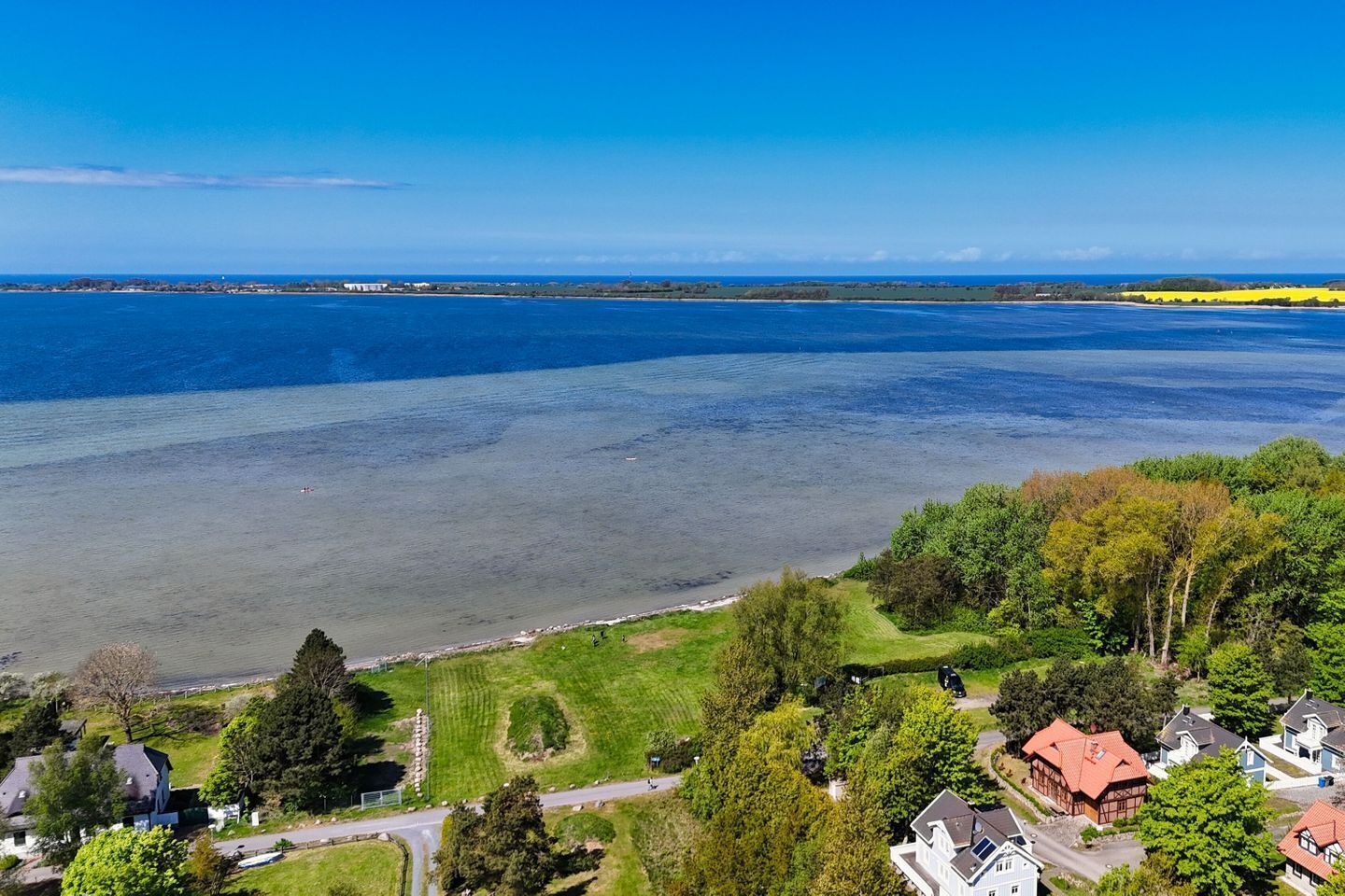 Een woongebied aan de kust, met huizen, een weg en een groot wateroppervlak.