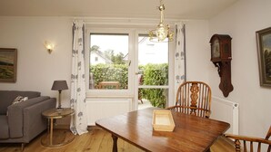 Ein Essbereich mit einem Holztisch, Stühlen, einer Kandelaber, einer Couch, einer Lampe, einer Uhr und einem Fenster mit Vorhängen.