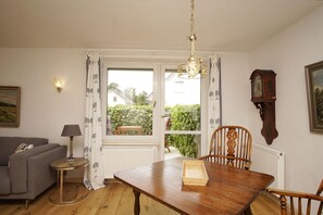 Ein Essbereich mit einem Holztisch, Stühlen, einer Kandelaber, einer Couch, einer Lampe, einer Uhr und einem Fenster mit Vorhängen.