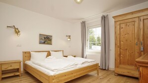 Ein Schlafzimmer mit einem hölzernen Bett, Nachttischen, einem Kleiderschrank, einem Fenster mit Vorhängen und Wandleuchten.