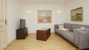 Ein Wohnzimmer mit grauem Sofa, einer Holzkommode, einem Glastisch und zwei Bildern an der Wand.