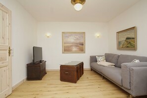 Ein Wohnzimmer mit grauem Sofa, einer Holzkommode, einem Glastisch und zwei Bildern an der Wand.