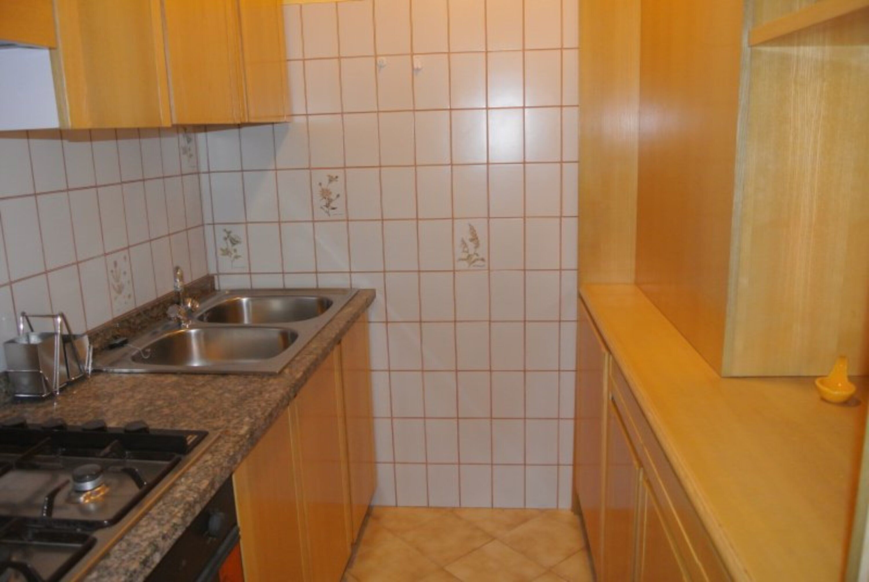 Une cuisine équipée d’une cuisinière à gaz, de deux éviers et d’un crédence carrelée.