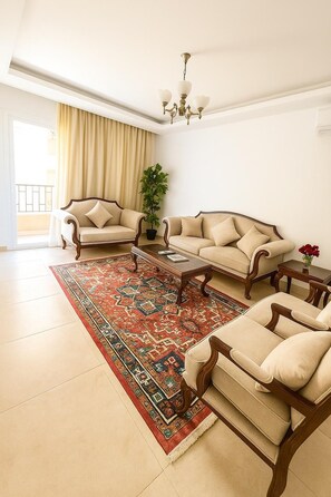 A spacious living room with a large rug, two sofas, a coffee table, and a chandelier. - Modern 2-Bedroom Apartment with Private Building Pool - ST4 (Giza)