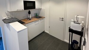 Une cuisine compacte avec des meubles blancs, un four à micro-ondes, un grille-pain et une petite table avec une bouilloire.