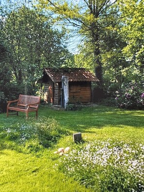A rustic wooden cabin with a bench in a lush garden.