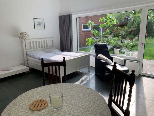 A bedroom with a bed, a chair, a table with a candle, and a view of a garden through a sliding door.