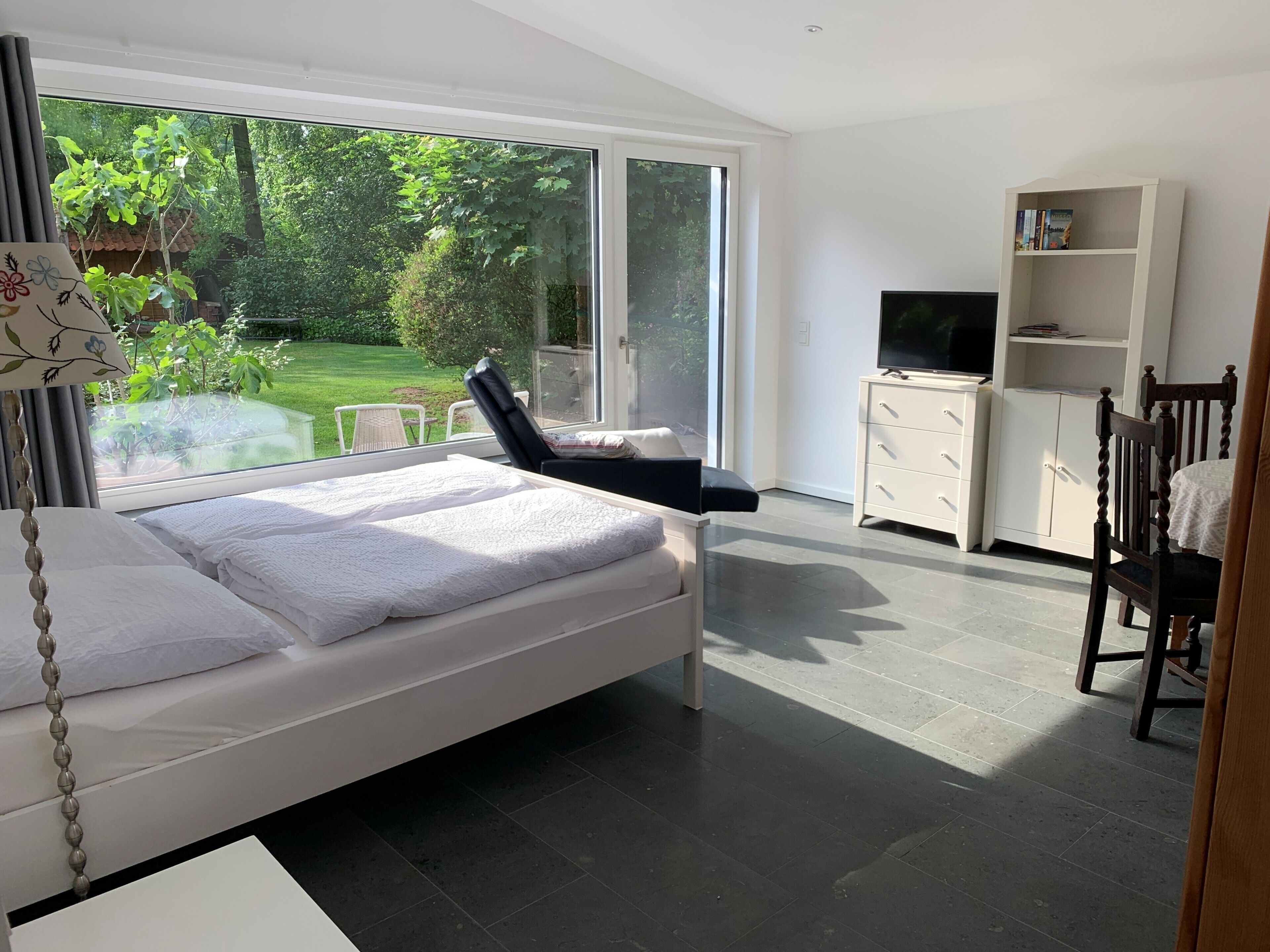 A modern bedroom with a bed, a TV, a bookshelf, and a view of a garden.. Vacation apartment Heske, 37 m², 1-2 pers.