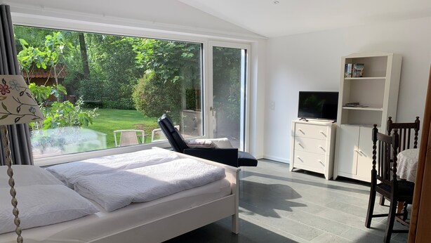 Une chambre moderne avec un lit, une télévision, une bibliothèque et une vue sur un jardin.