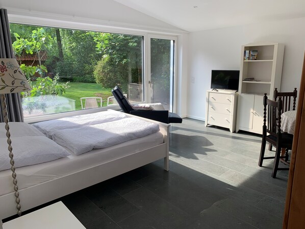 Une chambre moderne avec un lit, une télévision, une bibliothÚque et une vue sur un jardin.