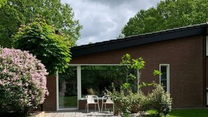 Un bâtiment moderne à l’extérieur en briques, doté d’un patio couvert avec des chaises et d’une pelouse bien entretenue.