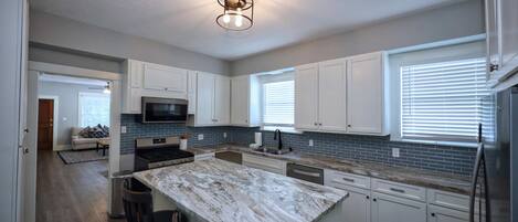 A modern kitchen with white cabinets, a granite island, stainless steel appliances, and a ceiling light fixture.